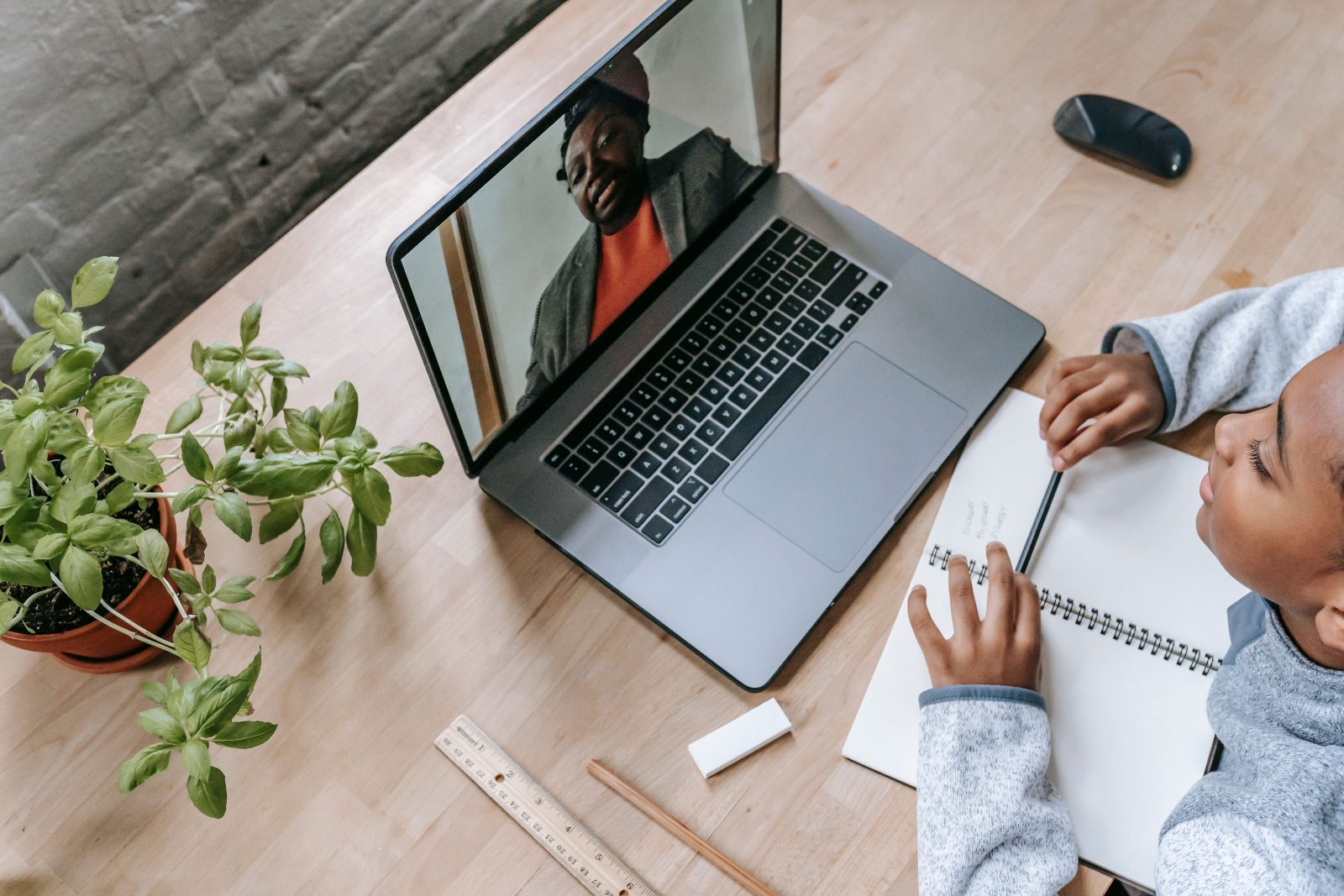 A student on a video-call tutoring lesson, taking notes while their tutor teaches from the laptop screen